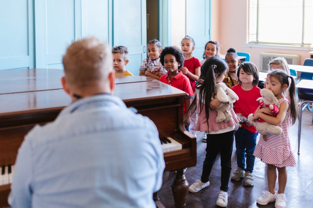 Teacher playing piano with young children watching