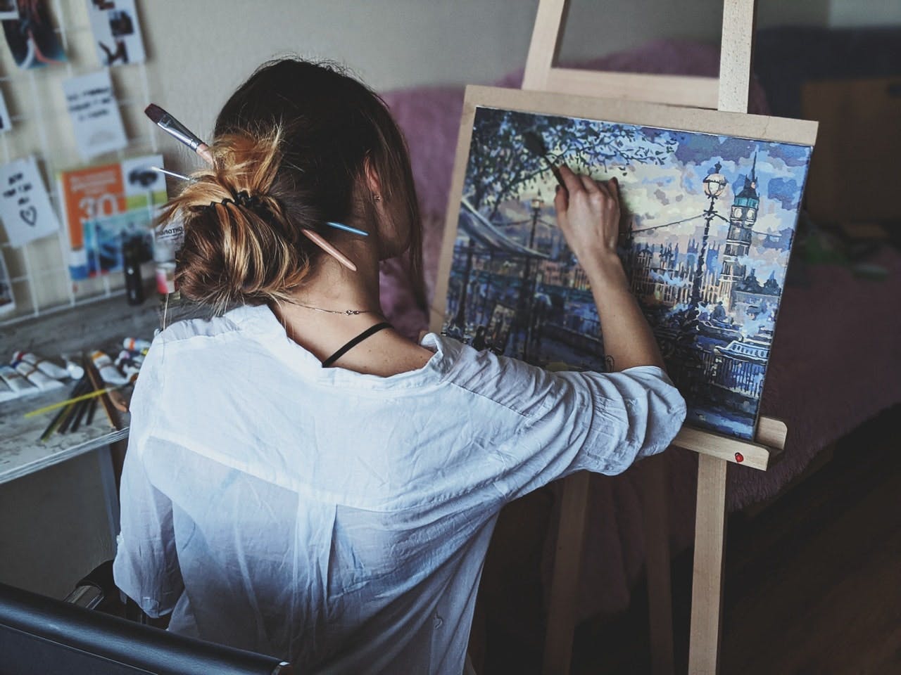 Young lady facing canvas on easel painting landscape