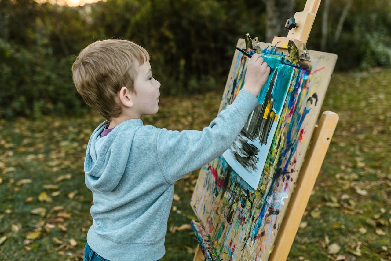 Young boy painting at easel outside